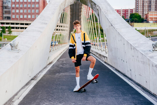 Caucasian teenager with skateboard standing on the bridge in the city
