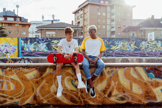 Two handsome teenage thoughtful boys with skateboard sitting on the wall on the street