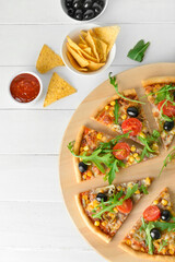 Board with slices of tasty pizza, sauce and nachos on light wooden background