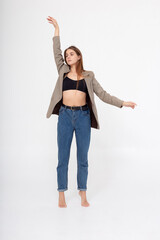 portrait of young caucasian attractive woman with long brown hair in blue jeans, black top and suit jacket on white background. skinny pretty lady posing at studio with bare feet