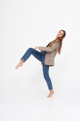 Obraz na płótnie Canvas portrait of young caucasian attractive woman with long brown hair in blue jeans and suit jacket on white background. skinny pretty lady posing at studio with bare feet