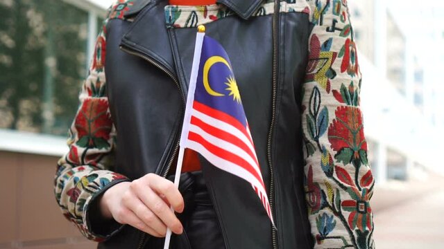 Unrecognizable woman holding Malaysian flag. Girl walking down street with national flag of Malaysia
