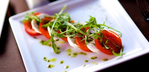 Salad with tomatoes and cheese on a white plate with arugula. Arugula lettuce leaves are on top of tomatoes and cheese. Delicious diet salad from the chef of the restaurant, light lunch