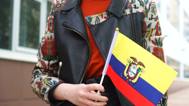 Unrecognizable woman holding Ecuadorian flag. Girl walking down street with national flag of Ecuador