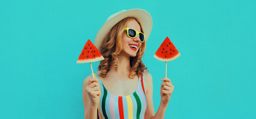 Summer portrait of happy smiling young woman with lollipop or ice cream shaped slice of watermelon wearing a straw hat on a blue background