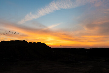 Sand mountain peaks and June evening sunset. Orange sky, clouds.