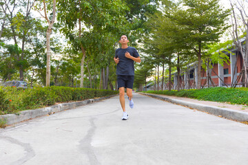 young sporty asian man running at road cover with green tree.