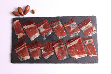 Portion of 100% acorn-fed Iberian ham Dehesa de Extremadura on a slate plate decorated with acorns and a white background viewed from above