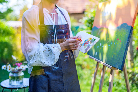 Beautiful young woman relaxing while painting an art canvas outdoors in her garden. Mindfulness, art therapy, creativity concept.