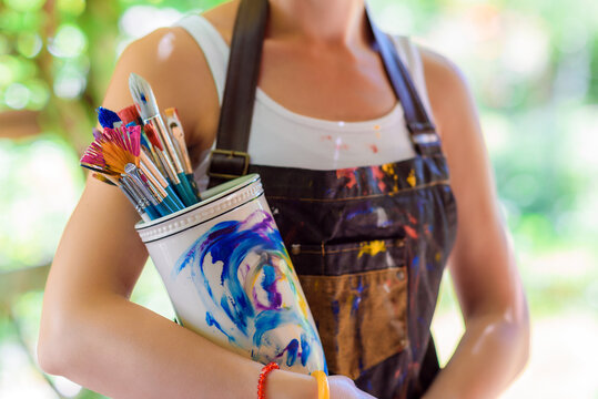 Young female painter artist holding a bunch of dirty used paintbrushes. Funky lifestyle creative hobbies background.