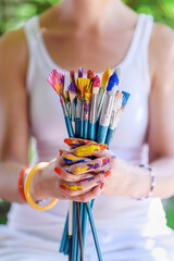 Young female painter artist holding a bunch of dirty used paintbrushes. Funky lifestyle creative hobbies background. © andreaobzerova