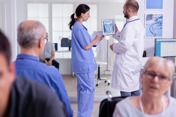 Obraz premium Specialist doctor examining radiography with hopistal nurse writing test result on clipboard. Medical staff working at disease treatment against virus infection standing in hospital waiting area