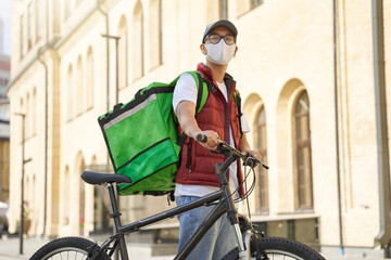 Young asian male courier with thermo bag wearing face protective