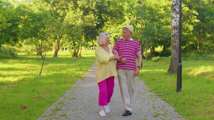 Obraz premium Senior stylish couple grandmother grandfather walking and talking in summer park. Happy old family husband, wife enjoying time together after retirement. Active elderly man pensioner walks with woman