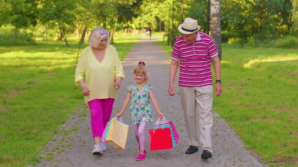 Child girl kid walking with senior grandmother grandfather with colorful bags after shopping....