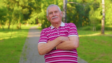 Naklejka premium Happy stylish senior old gray-haired man in casual red t-shirt posing isolated on summer park background. Active life after retirement. Lovely elderly smiling grandfather pensioner looking at camera