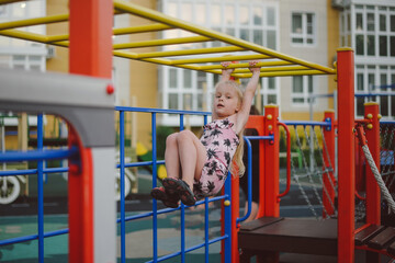 Obraz premium girl hanging on a horizontal bar in the playground in summer
