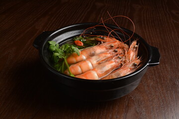 big tiger prawn poached with hot herbal soup and vegetables in black clay pot on wood table asian...