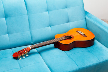 Classical guitar laying on a blue sofa, left behind, nobody around, closeup. Practicing a musical...