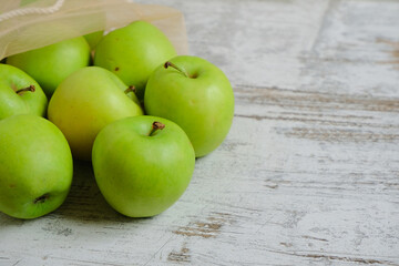 A part of eco bag with green fresh bright organic apples on a light natural wooden background. Apple template for your business. Empty space for your text or design.