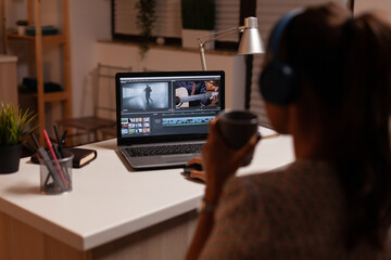 Filmmaker editing video footage during night time in home kitchen. Content creator in home working...