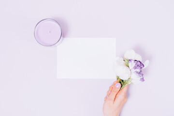 Flat lay blank white card next to woman's hand holding bouquet of fresh flowers