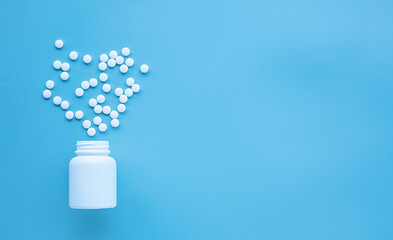 Flat lay of white tablets spilling from white plastic bottle on blue background with copy space. Minimal style concept. 