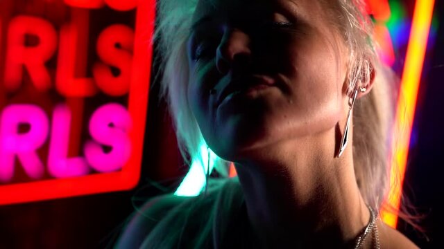 ortrait of a blonde with long hair in a dark room with neon signs. she touches lips with finger. contour light