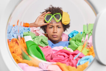 Serious attentive young woman with Afro hair wears snorkeling mask poses through washing machine...