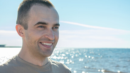 Young happy man the sea or the ocean background, guy looks thoughtfully into the distance, portrait, 16:9