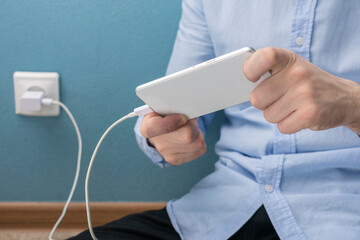 Man is playing games on the phone when it is charging, charger with cable, cropped image, close-up