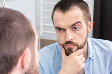 Obraz premium Handsome bearded man looking himself in bathroom mirror, portrait, close-up