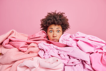Shocked young African American woman sticks head through pile of laundry stares stunned at camera...