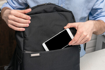 Person pulls a smartphone out of his backpack, man's hands, cropped image, close up, copy space