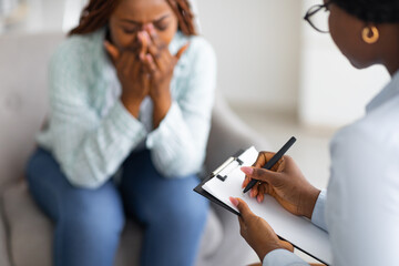 Stressed African American woman consulting psychologist, crying at medical office, selective focus