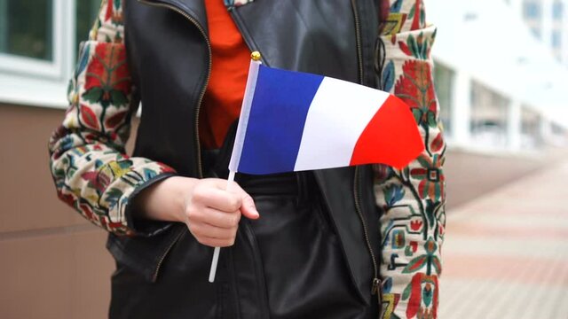 Unrecognizable woman holding French flag. Girl walking down street with national flag of France