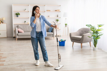 Cheerful woman talking on phone cleaning floor with mop
