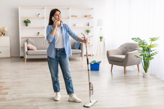 Cheerful Woman Talking On Phone Cleaning Floor With Mop