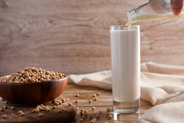 Soy milk in the glass by pouring from bottle with Soybean on wooden table background. Healthy foods...
