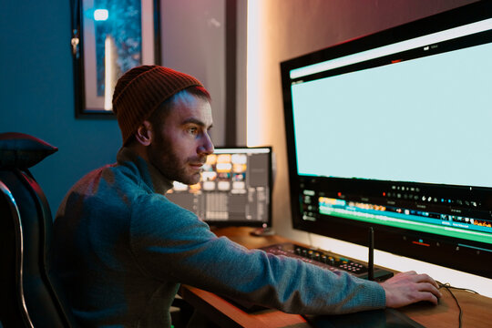 Attractive Male Video Editor Works with Footage or Video on His Personal Computer, he Works in Creative Office Studio or home. Neon lights