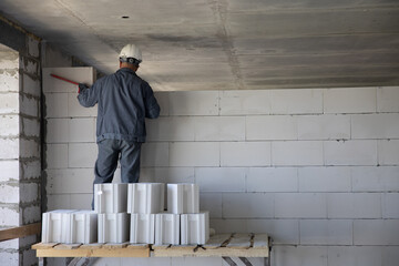 A worker in a hard hat puts a wall of large white bricks. The process of building a house....