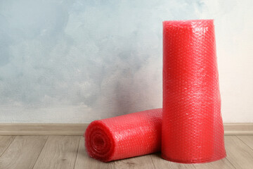 Red bubble wrap rolls on floor near light blue wall. Space for text