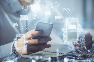 Double exposure of man's hands holding and using a digital device and envelop hologram drawing. E-mail concept.