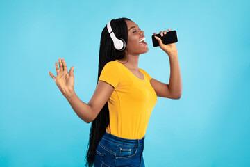 Happy Black Woman Singing Holding Smartphone Wearing Headphones, Blue Background
