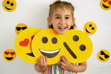 The girl holds cardboard smiley faces with different emotions in her hands: a sad, smiling happy...