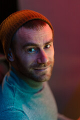 Neon light studio close-up portrait of smiling man with short mustaches and beard in his studio