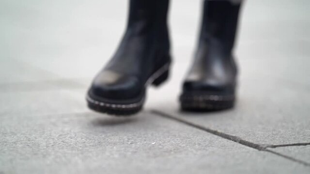 female feet in rough black boots step on the pavement tiles. small depth of field. the camera then shows a leopard print skirt and a leather backpack