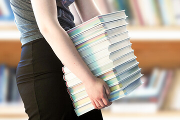 Back to school, hard to study. Girl holding a huge pile of books in the library