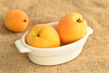 Three ripe organic yellow apricots with white ceramic dishes, close-up, on sacking.