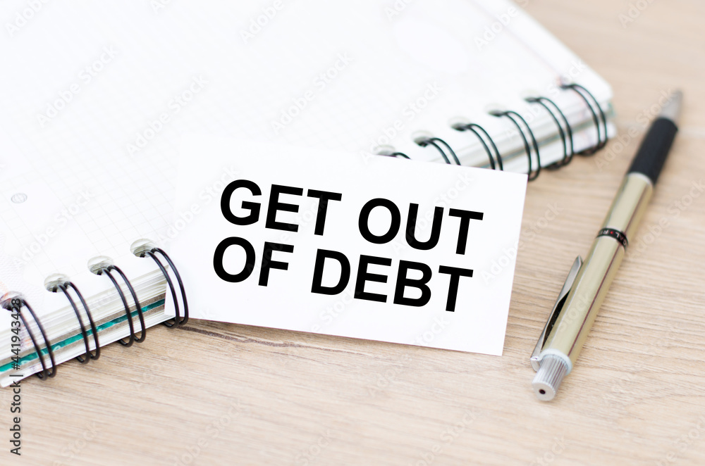 Poster card with text get out of debt on a wooden table next to a closed notebook